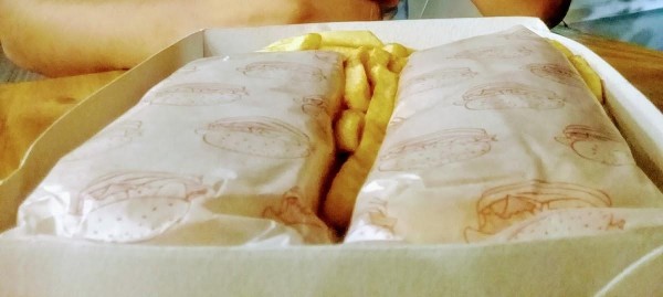 Pizza Piola: Dos empanadas envueltas en papel con dibujos, acompañadas de porciones de papas fritas en una bandeja blanca.