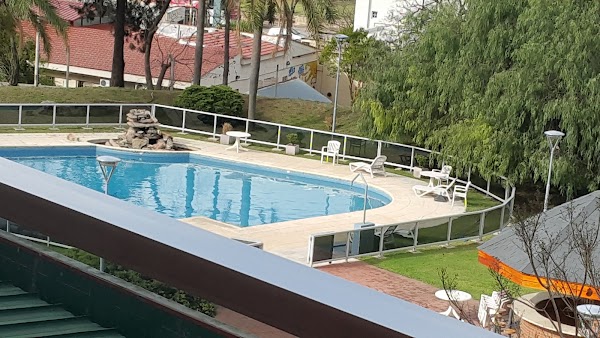 Piscina azul con tumbonas blancas rodeada de césped verde y árboles altos en Dr. César Carman.
