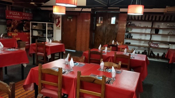 Interior de Carmelo Parrilla Restaurante: mesas con manteles rojos, sillas de madera y decoración rústica. Iluminación cálida.