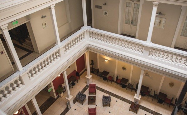 Hall con columnas blancas, balcones decorados y muebles rojos en el piso inferior. Iluminación cálida y ambiente elegante.