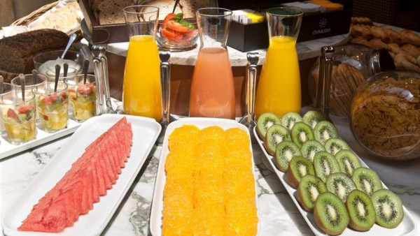 Desayuno en NH Urbano: frutas frescas, jugos coloridos y panes variados sobre mesa blanca.