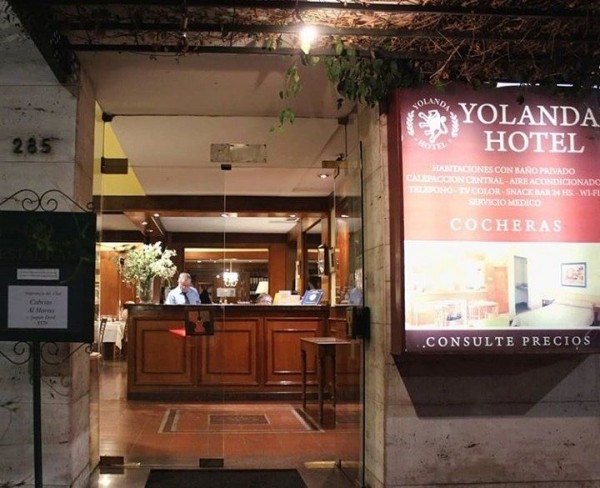 Entrada del Yolanda Hotel con recepción iluminada, cartel informativo y planta colgante. Ambiente acogedor y elegante.
