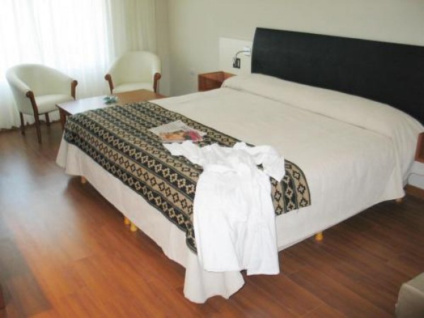 Habitación del Quorum Hotel & Spa con cama grande, sillas blancas y suelo de madera. Ambiente acogedor y elegante.