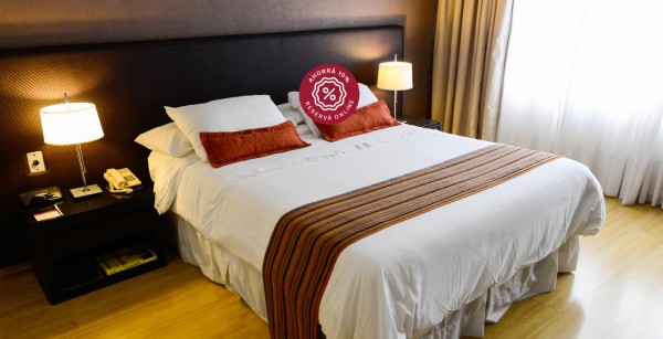 Habitación acogedora del Amerian Córdoba Park Hotel con cama grande, mesas de noche y cortinas beige. Iluminación cálida.