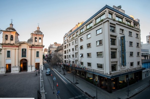 Hotel Windsor & Tower con fachada moderna y edificios históricos al fondo en una calle tranquila.