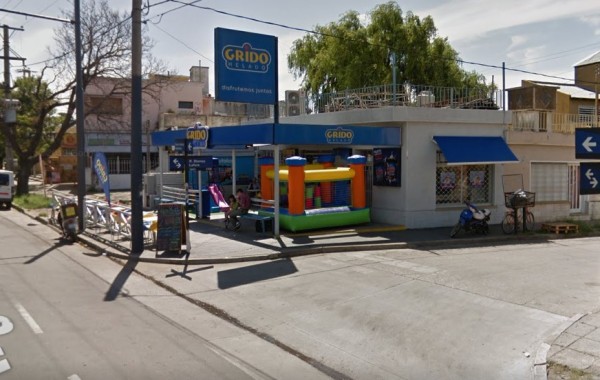 Estación Grido con inflable infantil colorido, bicicleta y motocicleta estacionadas frente a edificio blanco.