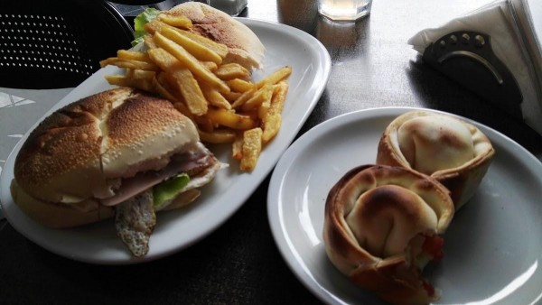 Pizzería Moma: hamburguesa con papas fritas y empanadas en platos blancos sobre mesa oscura.
