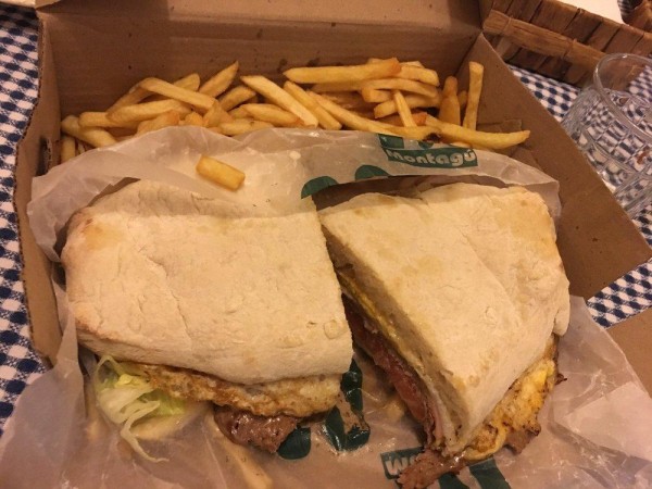 Sandwich de Montagú con carne y huevo, acompañado de papas fritas en caja abierta sobre mantel cuadriculado.