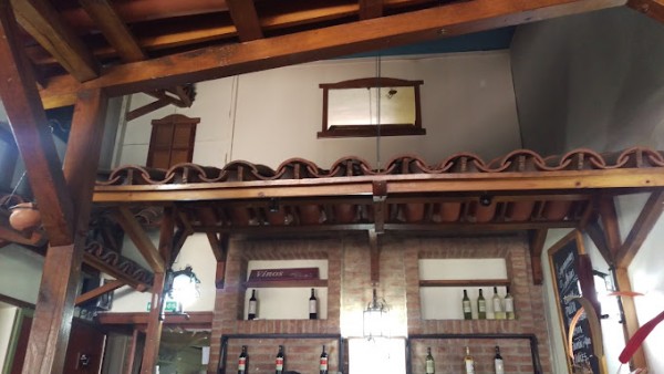 Interior con techo de madera, paredes de ladrillo, botellas de vino y decoración rústica.