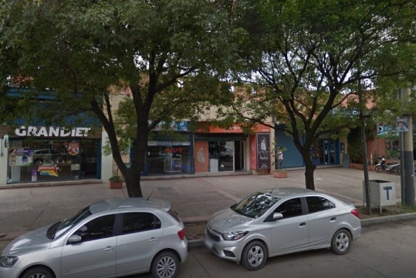 Calle con árboles y autos estacionados. Tiendas como 