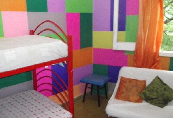 Habitación colorida del Hostel Joven con literas, sofá y cortinas naranjas. Ambiente acogedor y vibrante.
