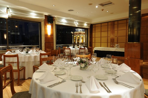 Restaurante elegante del Windsor Hotel & Tower con mesas blancas, sillas marrones y vista nocturna urbana.