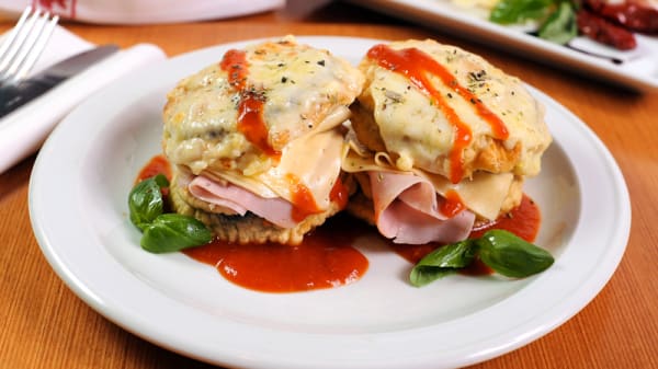 Plato de Il Gatto con dos montaditos de jamón y queso, salsa roja y hojas verdes sobre mesa marrón.