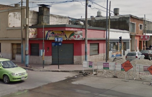 Pizzerías Franco: fachada roja con logo amarillo, calle con coches y señal de zanja abierta. Edificios al fondo.