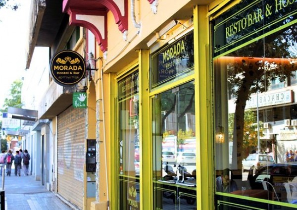 Fachada amarilla de Morada Hostel con grandes ventanales y letrero negro. Resto-bar visible desde la calle.