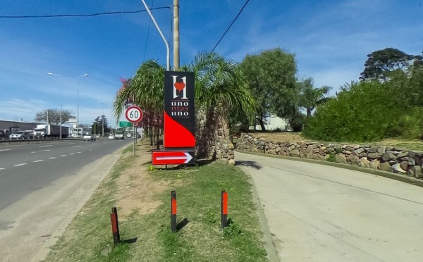 Entrada al Hotel Uno Mas Uno con cartel rojo y negro, camino pavimentado y vegetación alrededor.