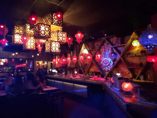 Bar con luces rojas, linternas colgantes y decoración geométrica colorida. Ambiente nocturno vibrante y acogedor.