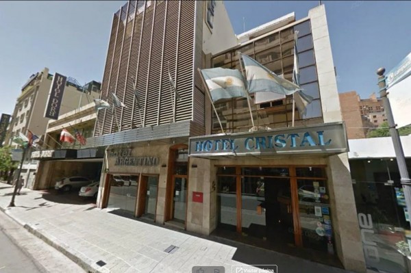 Hotel Cristal: fachada moderna con banderas argentinas, entrada principal y ventanas grandes. Edificio urbano en día soleado.