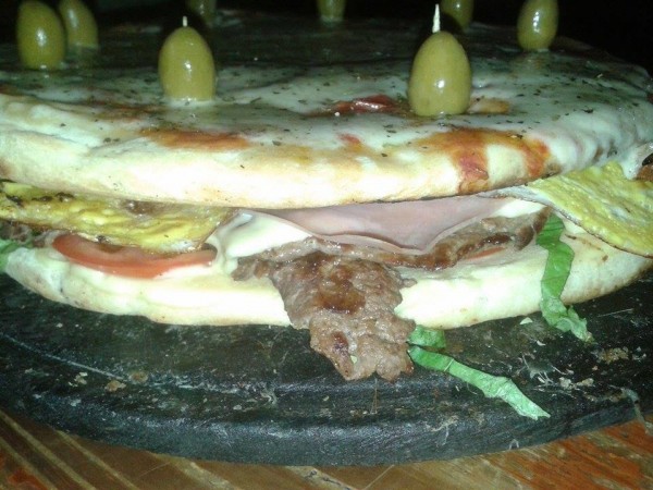 Pizza rellena con jamón, queso y carne, decorada con aceitunas verdes. Presentación creativa en Mr. Pizza.