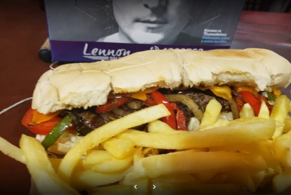 Sandwich con carne y verduras junto a papas fritas, frente a libro 