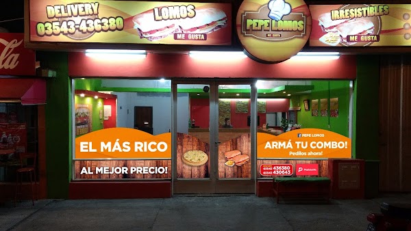 Fachada de Pepe Lomo con letreros luminosos, menú de combos y pizzas, y entrada principal iluminada.