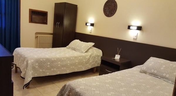 Habitación del Gran Savoy con dos camas individuales, armario, mesita y decoración moderna en tonos marrones y blancos.