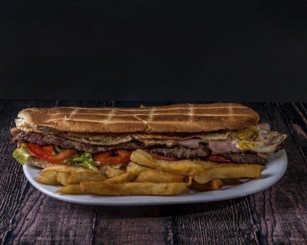 Sandwich gigante con carne, huevo y verduras, acompañado de papas fritas, en Pizzería La Juana.