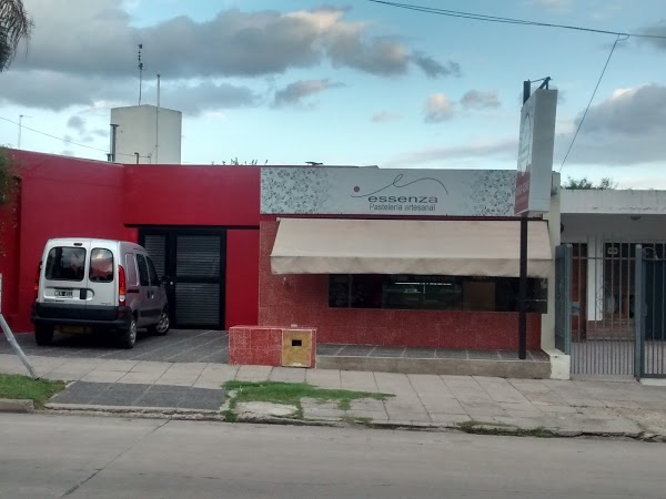 Fachada roja de Essenza Pastelería con toldo blanco y coche estacionado frente al local. Cielo nublado.
