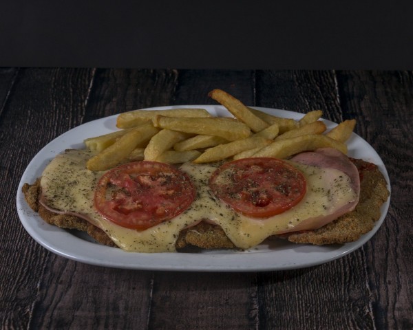 Milanesa con queso, tomate y jamón, acompañada de papas fritas en Pizzería La Juana. Plato apetitoso sobre mesa de madera.