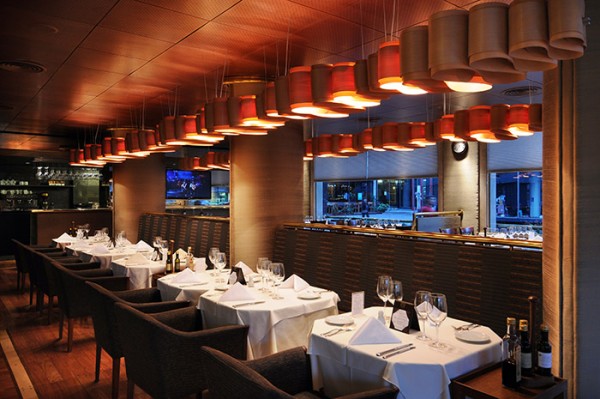 Restaurante Sibaris: mesas con manteles blancos, sillas negras y lámparas colgantes iluminando el ambiente elegante.