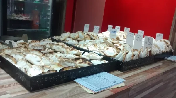 Exhibición de empanadas en mostrador de local gastronómico con etiquetas y refrigerador al fondo.
