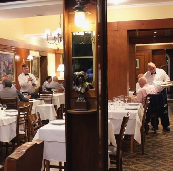 Restaurante elegante del Yolanda Hotel con mesas blancas, camareros atendiendo y decoración clásica.