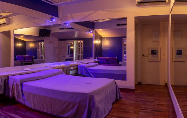 Hotel Uno Mas Uno: Habitación con camas blancas, iluminación azulada y puertas abiertas hacia áreas comunes. Ambiente moderno y acogedor.
