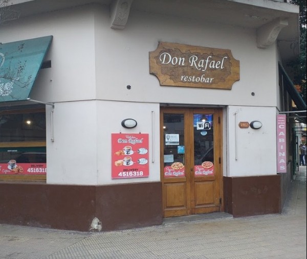Fachada de Don Rafael Resto Bar con puertas de madera, cartel publicitario y señal de WiFi. Edificio blanco con base marrón.