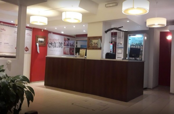 Recepción de Casa Criolla con mostrador marrón, luces colgantes y paredes rojas. Ambiente acogedor y moderno.