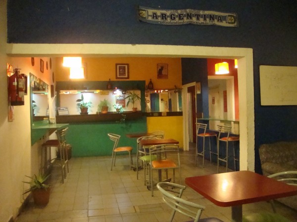 Interior RUNC Residencia Universitaria: bar con mesas, sillas y decoración colorida. Cartel 