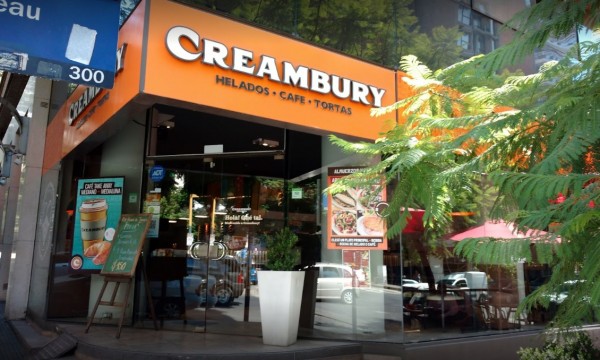 Creambury: heladería con fachada naranja, vidrios grandes y árboles frente. Ofrece helados, café y tortas.