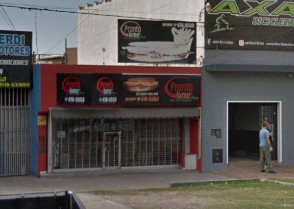 Fachada roja de Pizza Pronta con letrero y ventana cerrada. Persona camina junto a bicicletas. Edificio urbano.