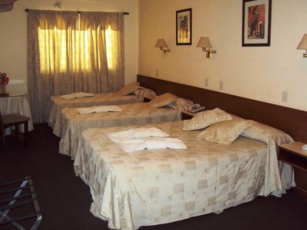 Habitación del Hotel Cristal con tres camas, cortinas amarillas y decoración clásica. Ambiente acogedor y cómodo.