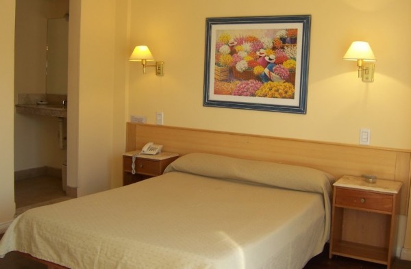Habitación acogedora del Yolanda Hotel con cama doble, mesitas de noche y cuadro floral sobre la pared beige.
