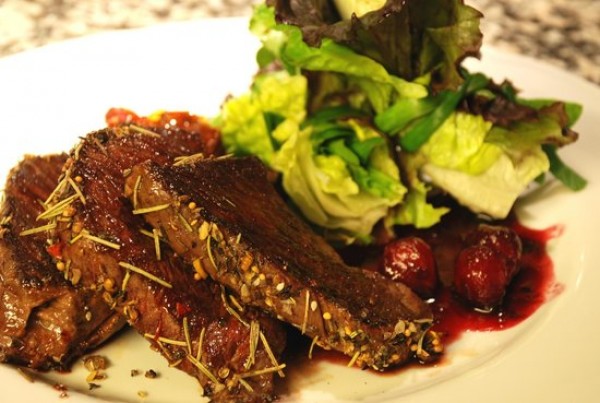Plato de Goulu: costillas de cerdo con hierbas, ensalada verde y salsa de cerezas rojas. Presentación gourmet.