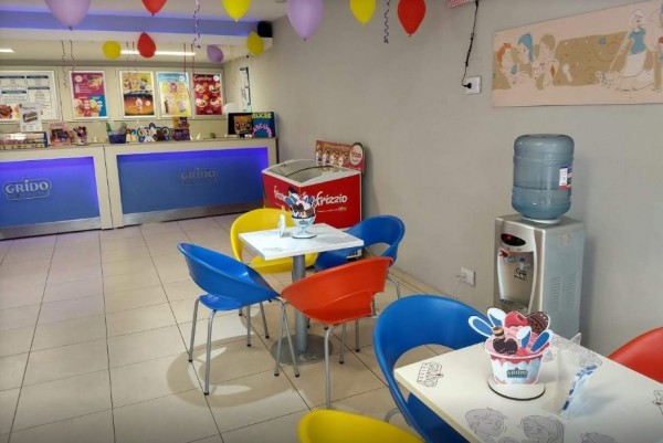 Interior de Grido con mesas coloridas, helados, globos y decoración infantil. Ambiente alegre y acogedor.