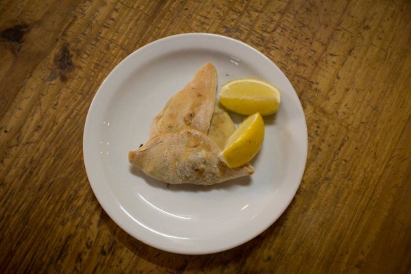 Plato blanco con empanadas y rodajas de limón sobre mesa de madera rústica en Macuba.