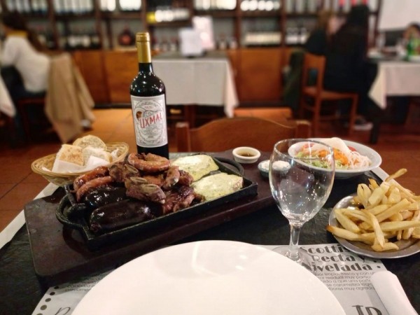 Asado y papas fritas en bandeja, acompañados de vino tinto y ensalada en 