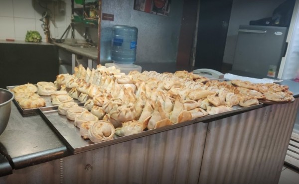 Mostrador con empanadas doradas y variadas en Pizza Margarita. Ambiente cálido, cocina visible al fondo.