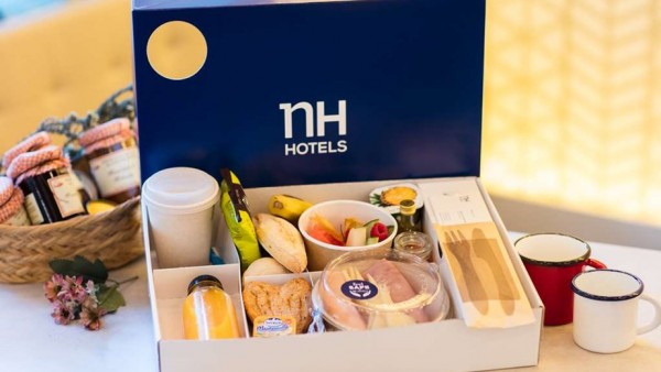 Caja de NH Hotels con desayuno: café, frutas, pan, mermelada y yogur. Ambiente acogedor en NH Urbano.