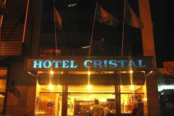 Hotel Cristal iluminado por la noche, con banderas ondeando y entrada principal brillante.