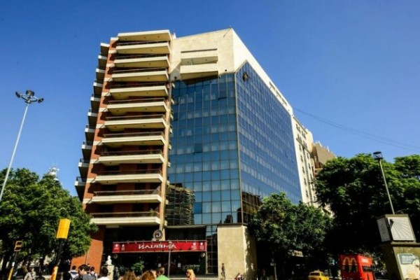 Edificio moderno con fachada de vidrio y balcones, rodeado de árboles verdes. Amerian Córdoba Park Hotel.