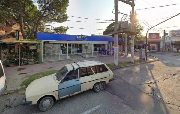 Auto antiguo estacionado frente a Grido, tienda con fachada azul y blanca, árboles y calles alrededor.