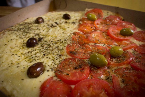 Pizza de Macuba con tomates, aceitunas verdes y negras, hierbas y queso derretido. Plato apetitoso y colorido.